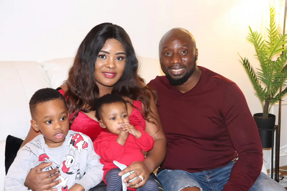 A family of four smiling together at home.