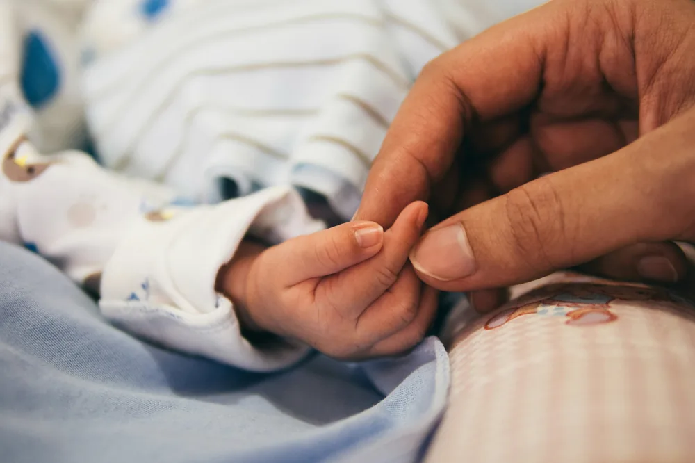A newborn baby holding a parent’s finger.